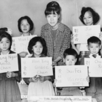 April Lou, teacher at Public School 1 in lower Manhattan, with six children who had recently arrived from Hong Kong and Taiwan in 1964, holding up placards giving his or her Chinese name (both in ideographs and in transliteration) and the name to be entered upon the official school records. Photo credit: Fred Palumbo.